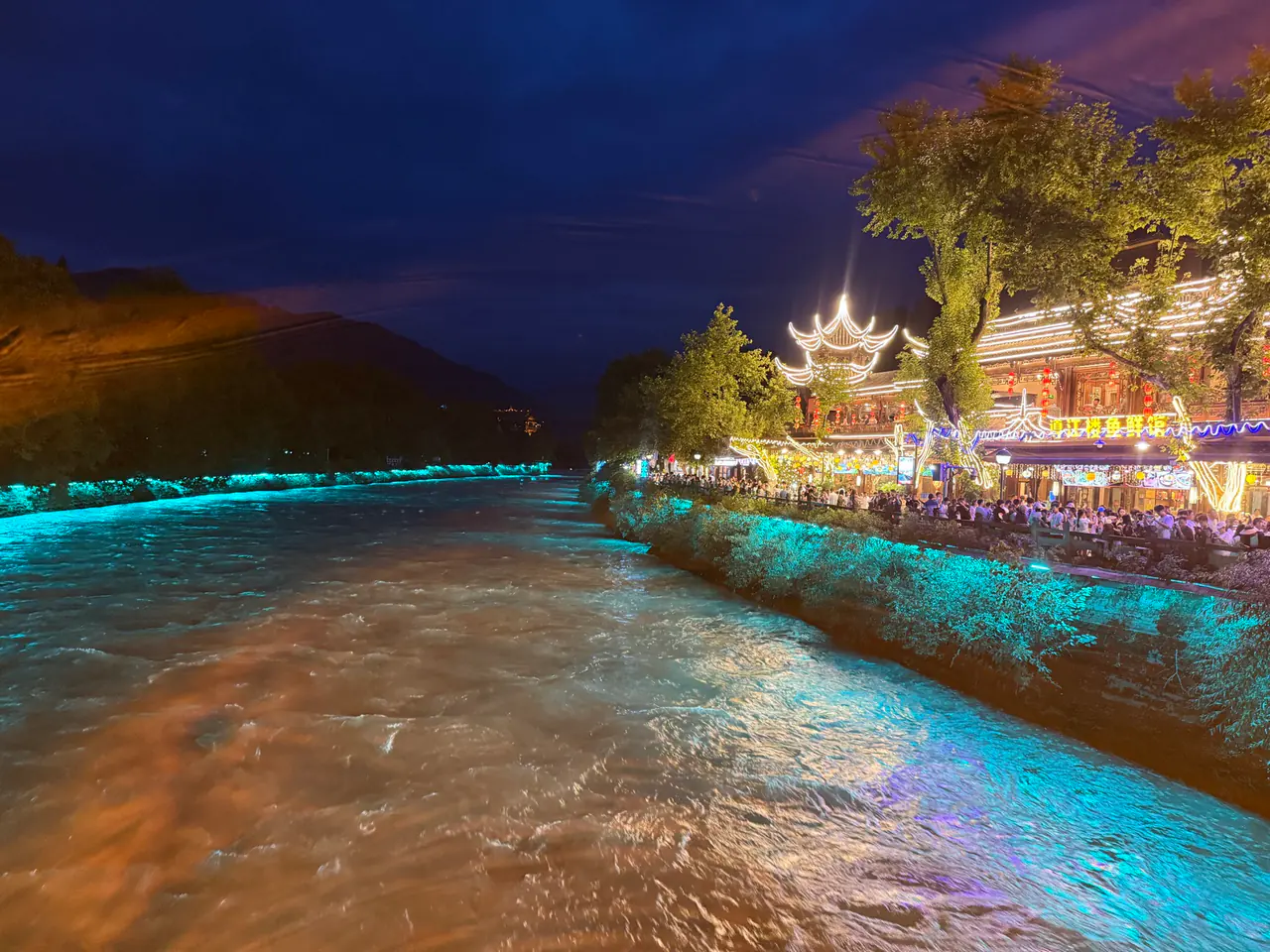 The Dujiangyan river glowing turquoise at dusk, with the lantern-lit old town along the far bank.